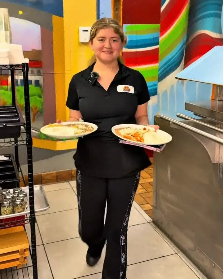A Camacho's server carrying two breakfast plates past the Ecatepec mural